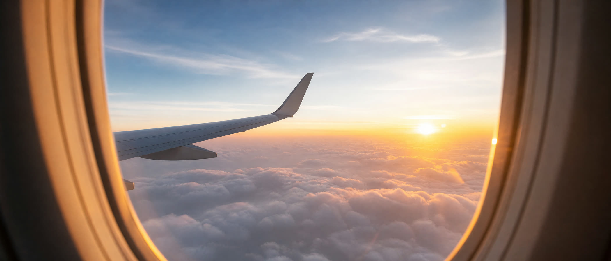 Airplane wing above sunrise clouds